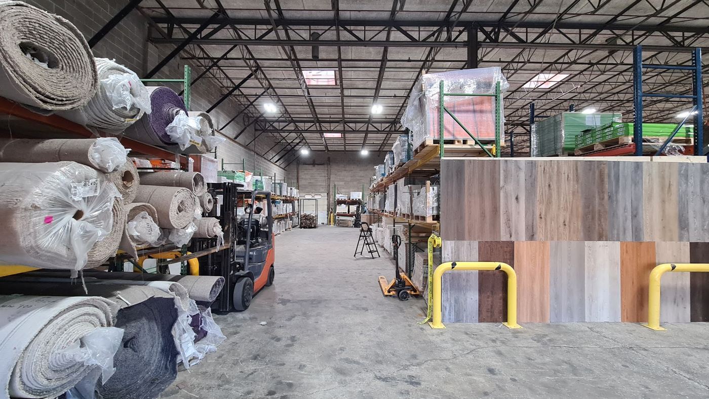 Warehouse aisle with carpet rolls on racks and a wall of flooring samples