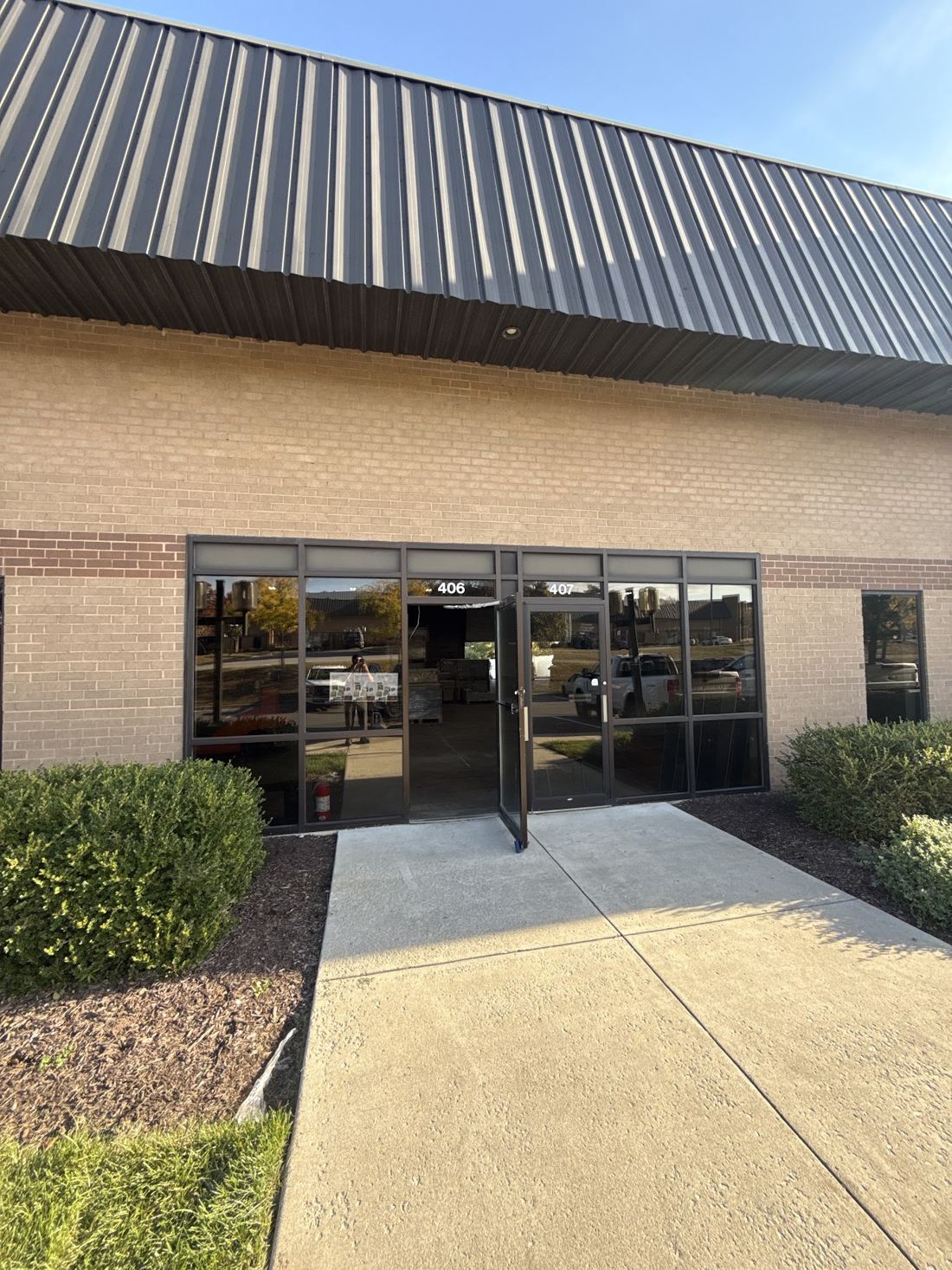 Contractors Supply entrance: tan brick building with a dark metal roof and glass doors marked 406